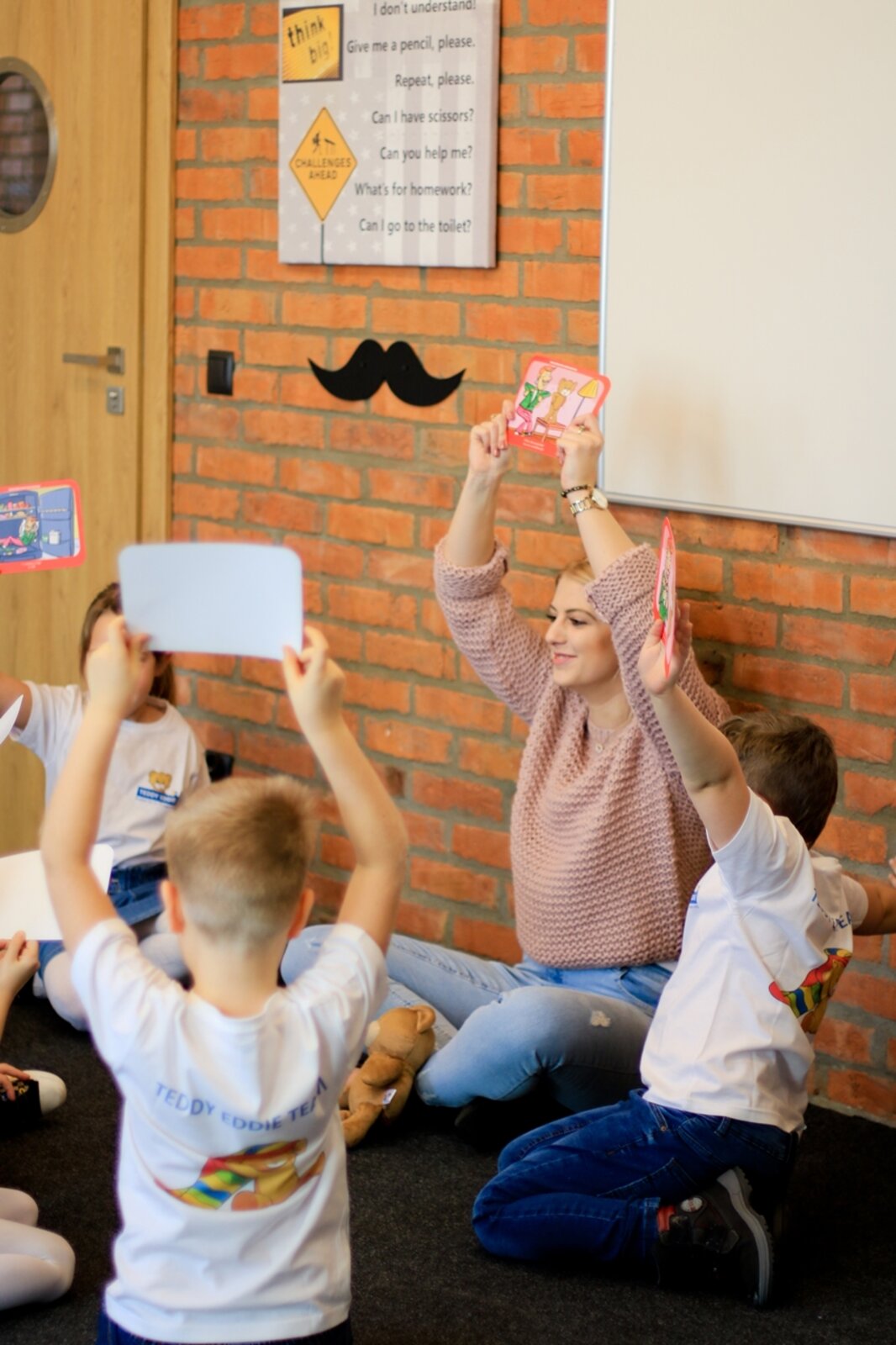 Lektorka prowadzi zajęcia Teddy Eddie z grupą dzieci, pokazując karty obrazkowe
